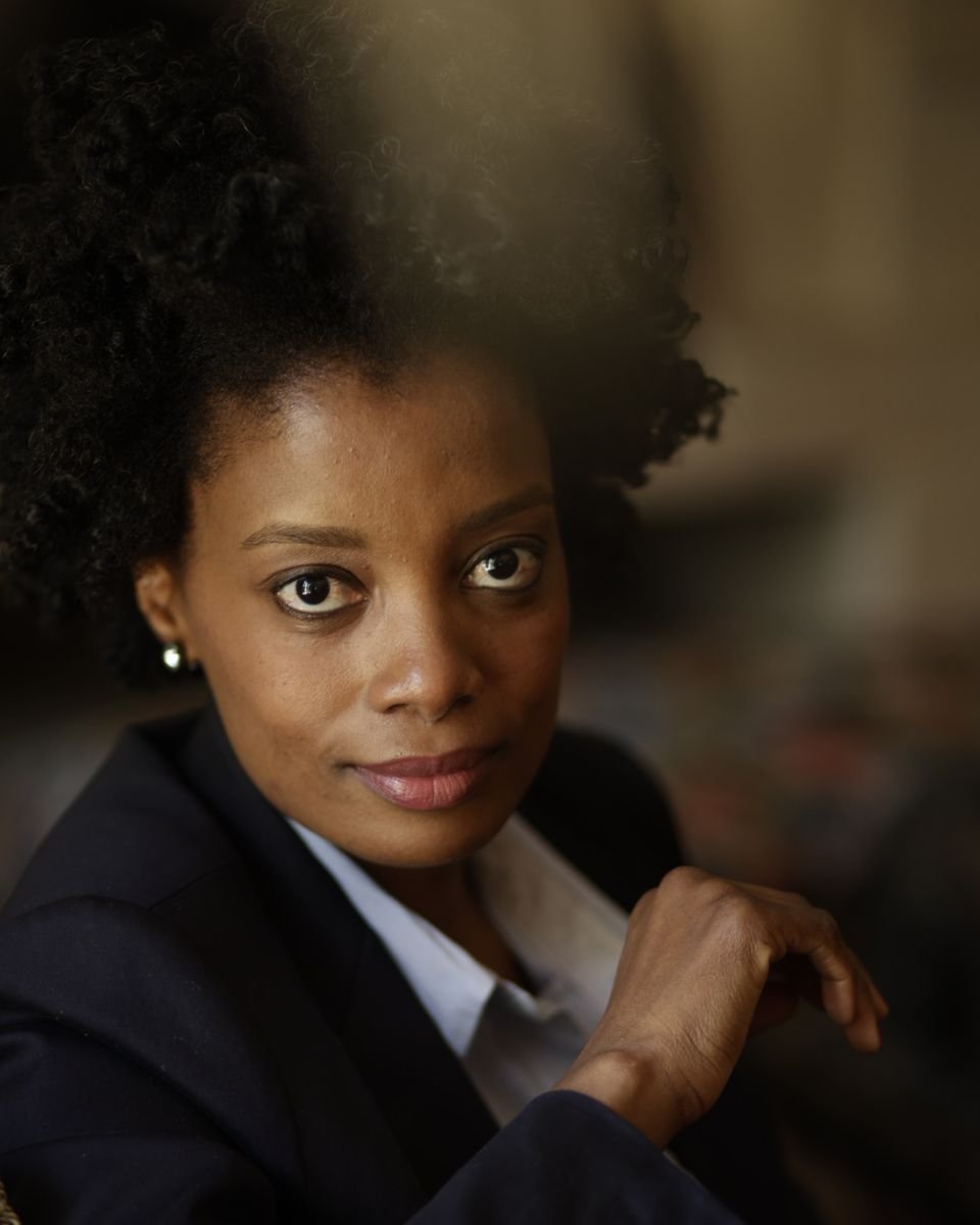 Maud Nale in a navy suit with a soft smile, hand raised